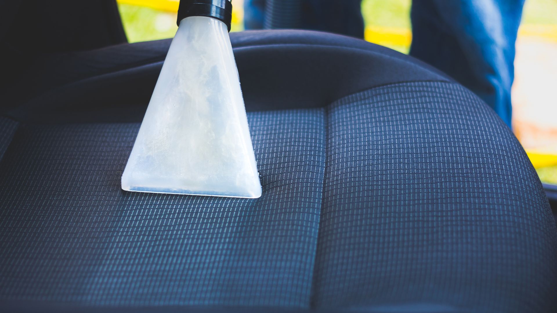 White cleaning attachment on car seat during professional upholstery cleaning