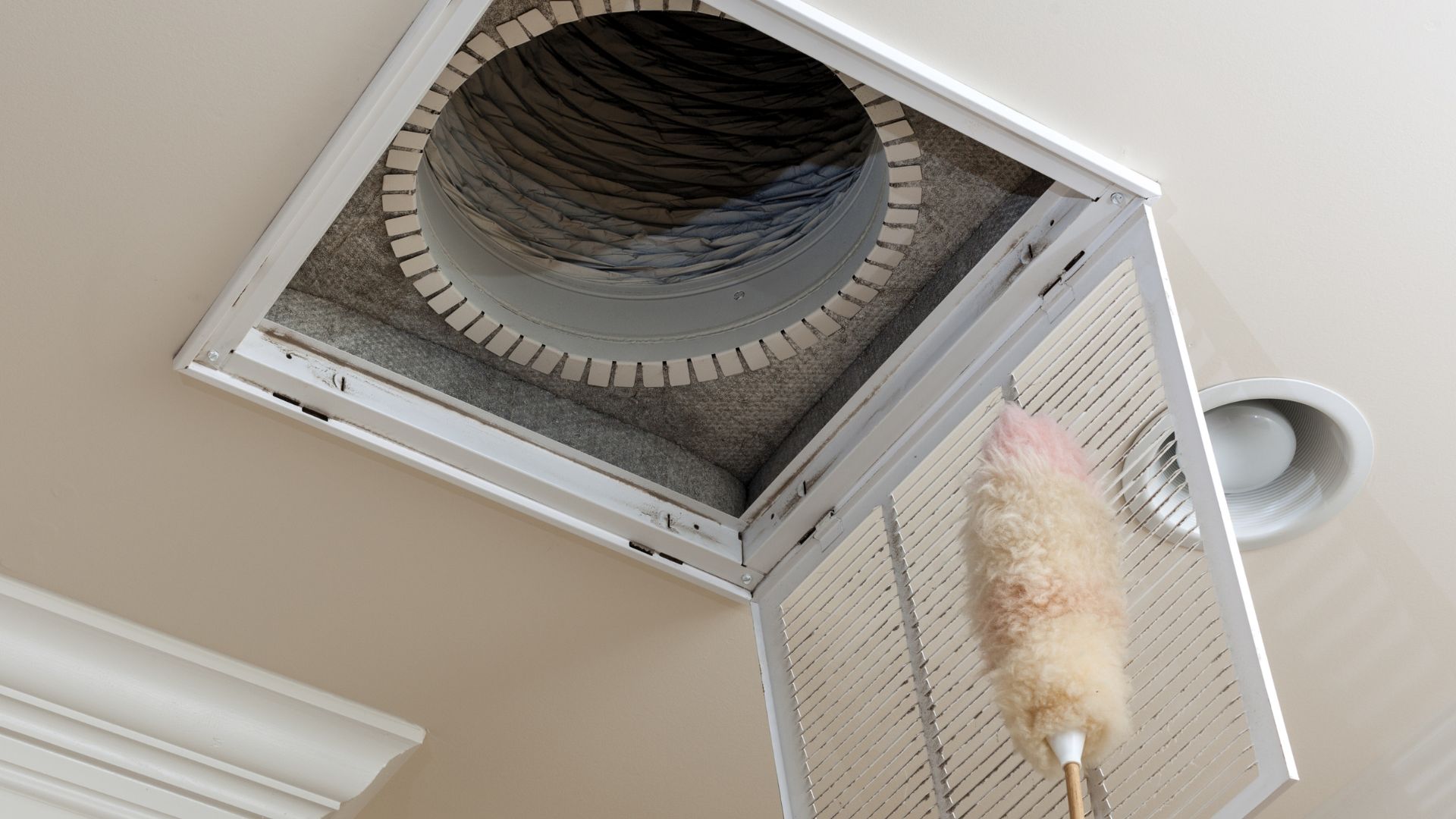 Dusting a ceiling air vent with a fluffy long-handled duster