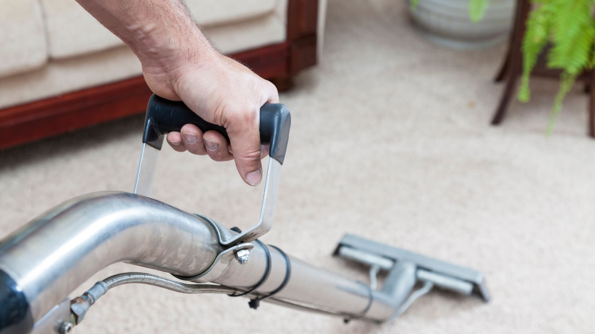 Hand holding vacuum cleaner attachment on carpeted floor