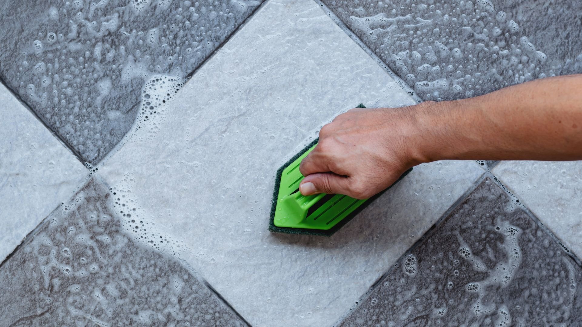 Hand using green sponge to clean wet tiled surface